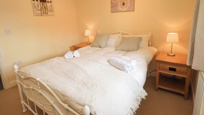 Cama bem arrumada com lençóis brancos, duas mesas de cabeceira com abajures e uma parede decorada com duas obras de arte.