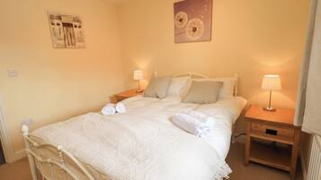 A neatly made bed with white linens, two bedside tables with lamps, and a wall with two pieces of artwork.