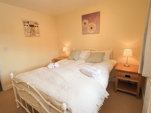 Un lit bien fait, avec du linge de lit blanc, deux tables de chevet avec des lampes et un mur orné de deux œuvres d’art.
