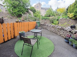 Un patio con una mesa redonda y dos sillas, rodeado por un muro de piedra y una valla de madera.