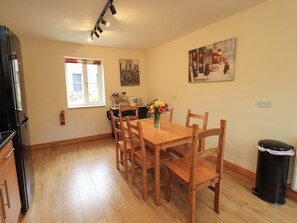 A dining area with a wooden table, chairs, a vase of flowers, a fire extinguisher, and a painting on the wall. - Mellbeck Retreat (Kirkby Stephen)