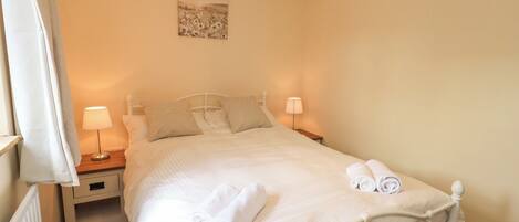 A neatly made bed with white linens and towels, two bedside lamps, a nightstand, and a painting on the wall.