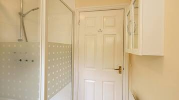 A bathroom with a shower, a white door, and a mirror.