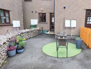 Une cour avec un mur en pierre, des plantes en pot, une table avec des chaises et une porte donnant sur une pièce.