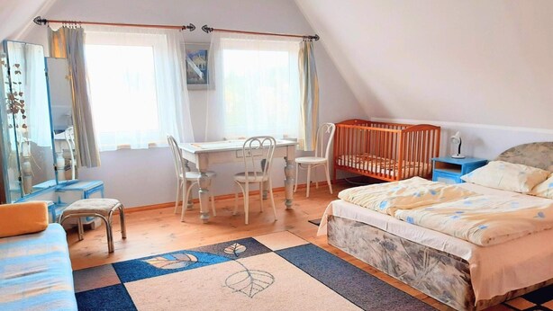 A bedroom with a bed, a crib, a desk with chairs, a mirror, and a window with curtains. - Large, Comfortable Holiday Home Near the Lake (Stawiguda)