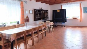A dining area with a wooden table and chairs, a black cabinet, and a large window with curtains. - Large, Comfortable Holiday Home Near the Lake (Stawiguda)