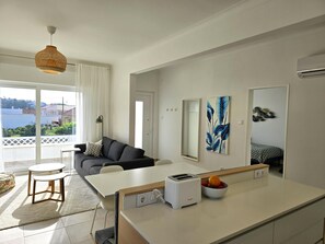 Ein modernes Wohnzimmer mit einer Couch, einem Esstisch und einer Küchenzeile inklusive Toaster und Obstschale.
