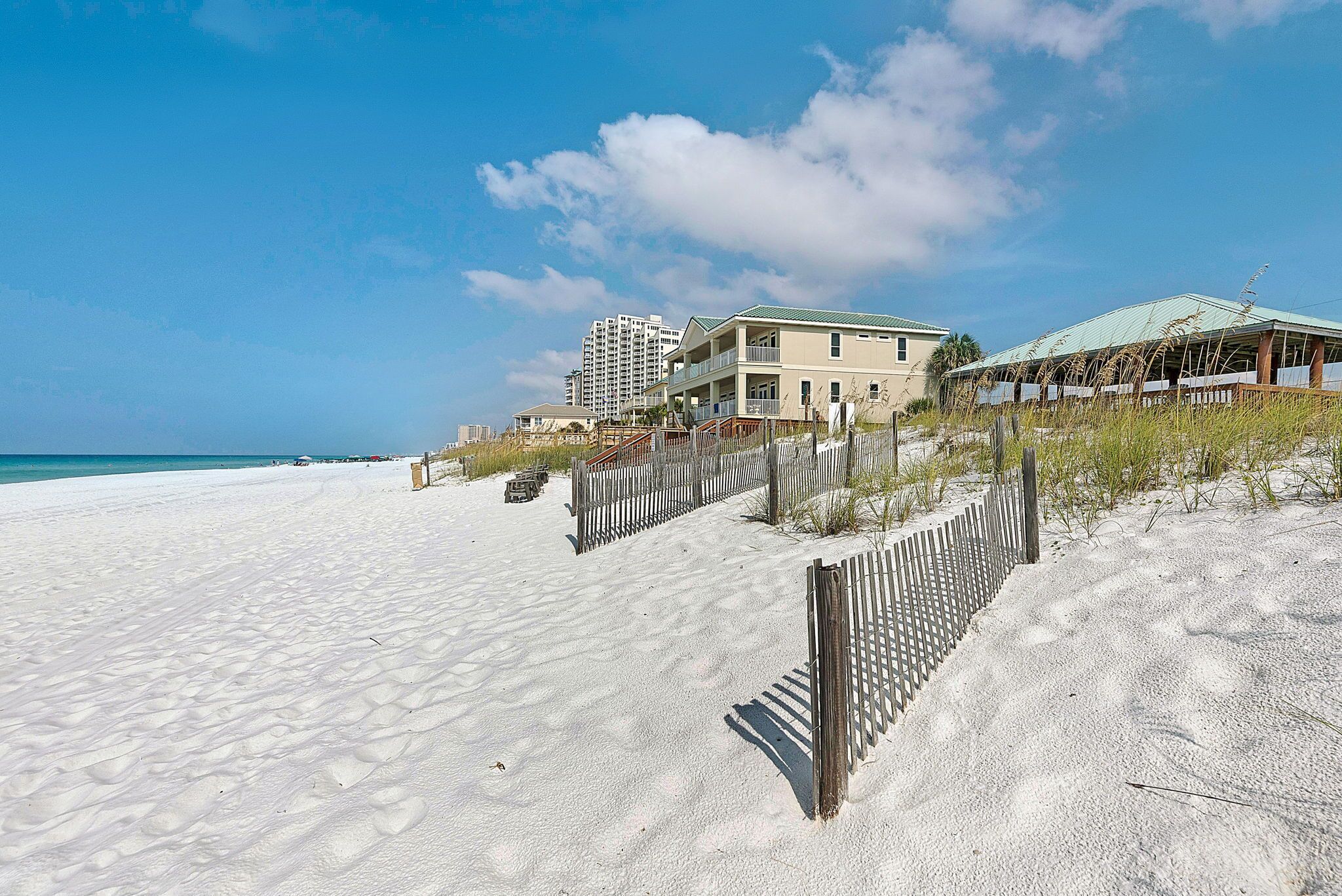 A beachfront property with a sandy beach, a wooden fence, and a building with a green roof.