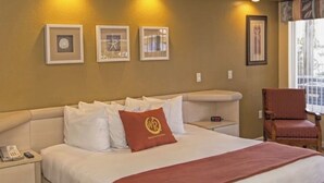 Habitación de hotel con cama, mesita de noche, una silla, ventilador de techo y cuadros en la pared.