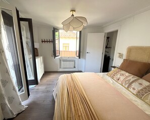 Un dormitorio con cama, un radiador, un ventilador de techo y una ventana con la puerta abierta.