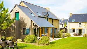A two-story house with a sloped roof, a wooden exterior, and a fenced backyard with outdoor furniture. - Coastal Apartment Escape in Cancale (Cancale)
