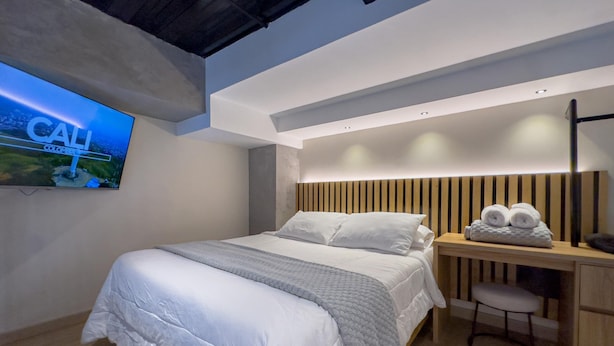 A modern bedroom with a large bed, a desk, and a television mounted on the wall.
