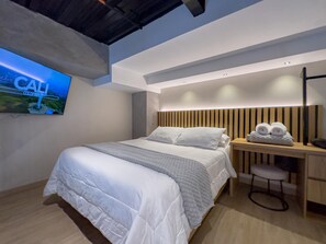 A modern bedroom with a large bed, a desk, and a television mounted on the wall.