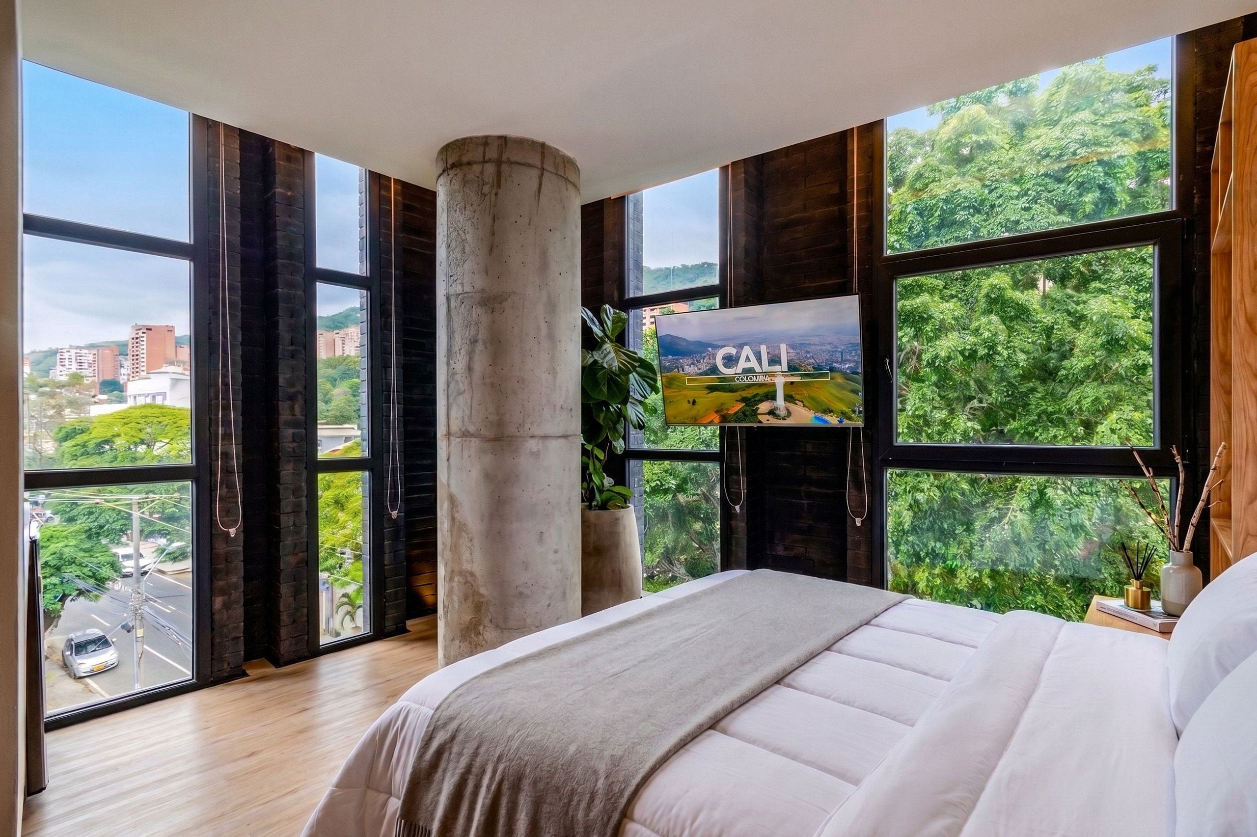 A bedroom with a large bed, a fireplace, and a cityscape view through large windows.