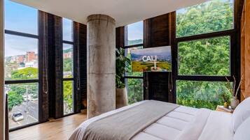 A bedroom with a large bed, a fireplace, and a cityscape view through large windows.