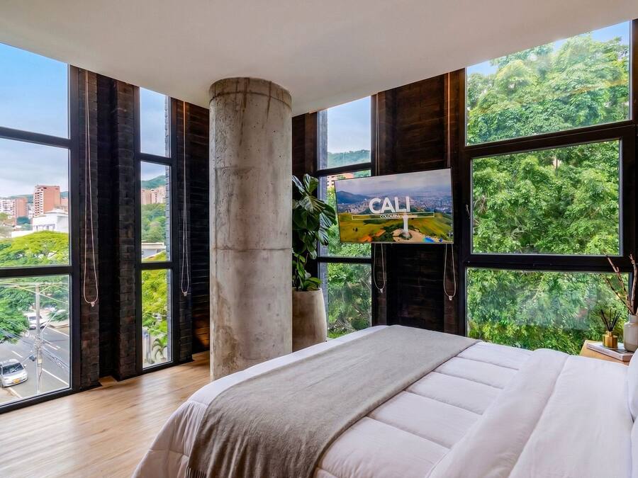 A bedroom with a large bed, a fireplace, and a cityscape view through large windows.