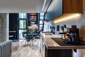 Una cocina moderna con cafetera, zona de comedor con sillas y un ventanal grande.
