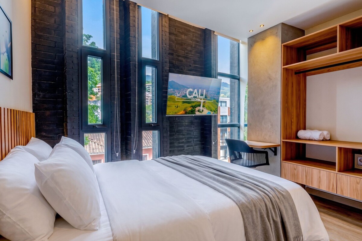 A modern hotel room with a large bed, a desk, and a TV displaying a scenic view.
