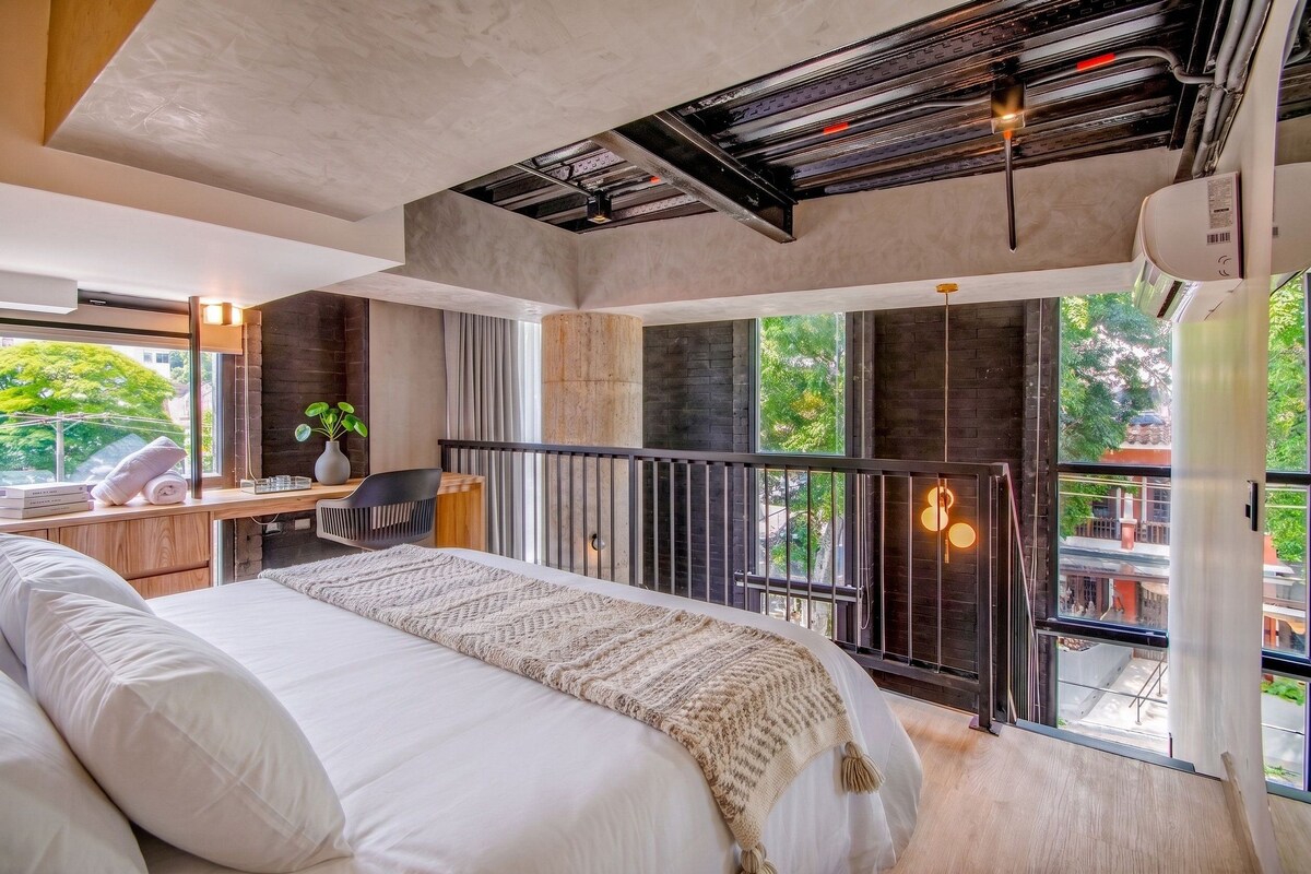 A modern bedroom with a large bed, a desk, and a balcony with a view.