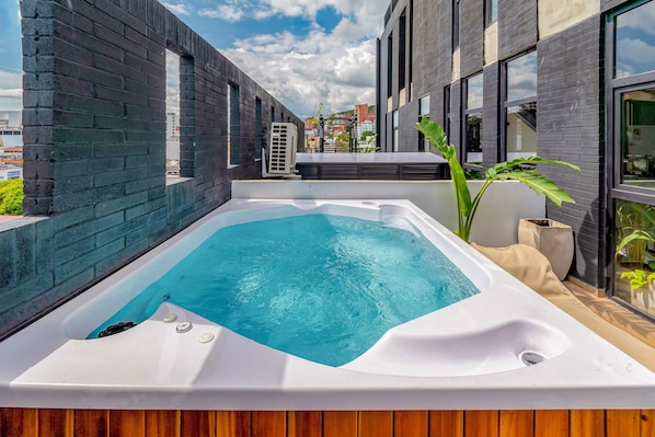 A rooftop swimming pool with a wooden deck, surrounded by modern buildings.