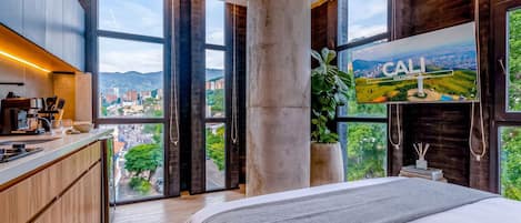 A modern hotel room with a large bed, a kitchen area, and a TV displaying a view of Cali, Colombia.