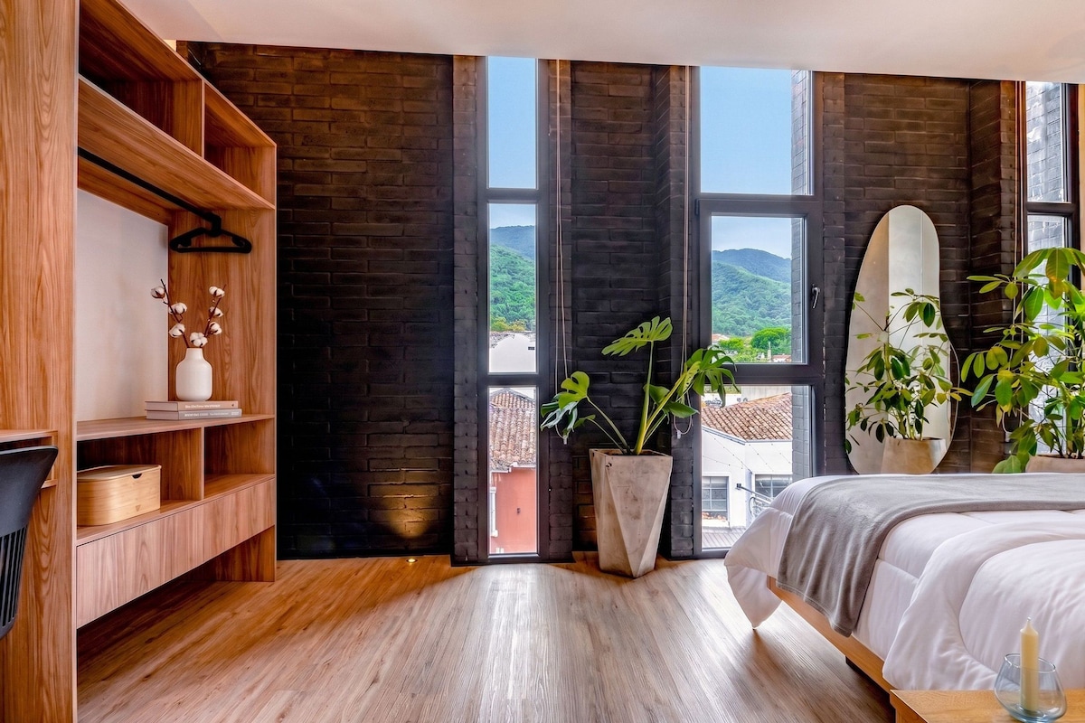 A modern bedroom with a large bed, wooden shelving, and a view of a mountainous landscape through large windows.