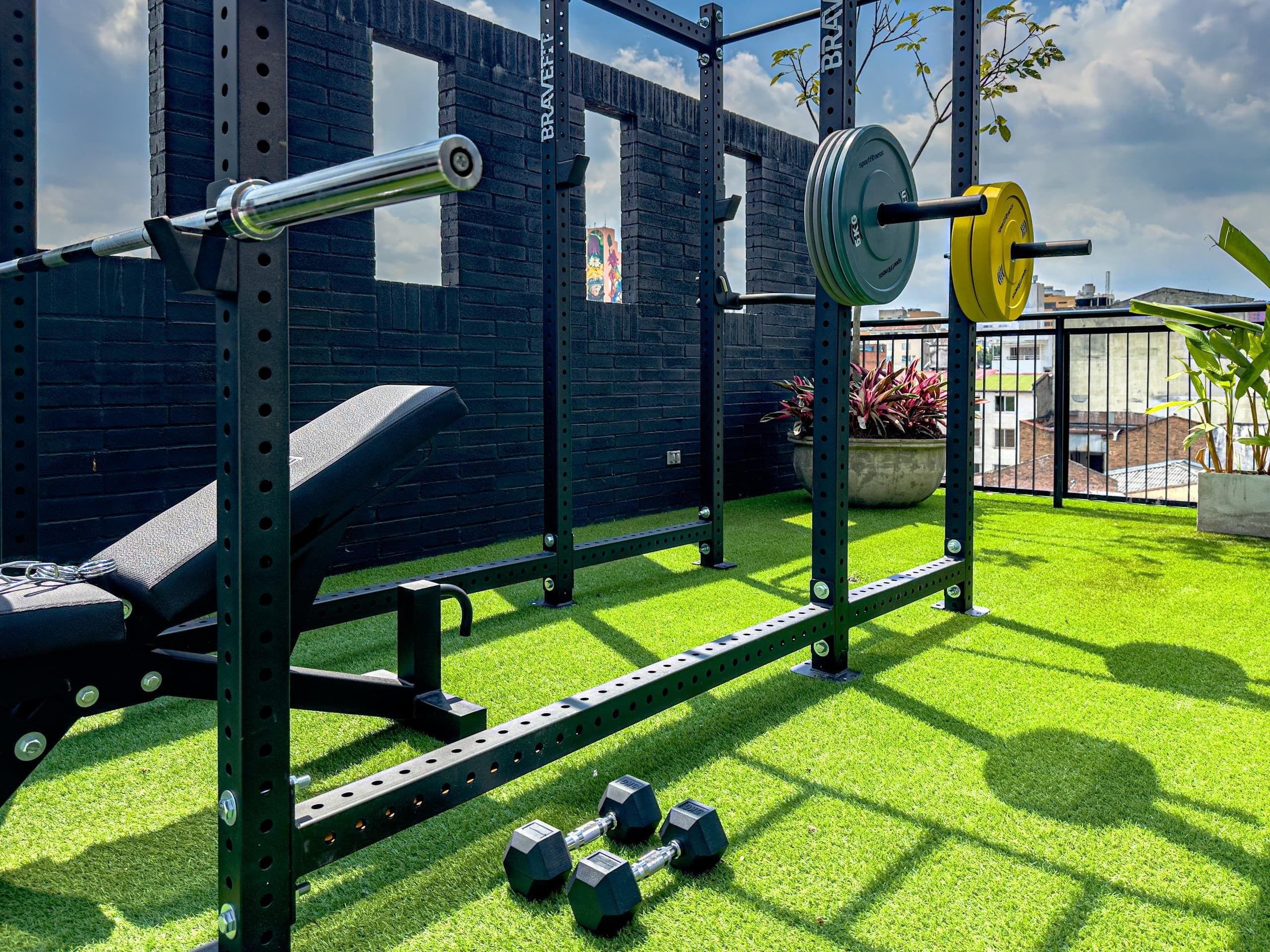 A weightlifting area with a squat rack, barbell, and dumbbells on artificial grass.