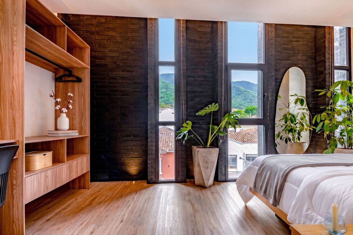 A modern bedroom with a large bed, wooden shelving, and a view of a mountainous landscape through large windows.