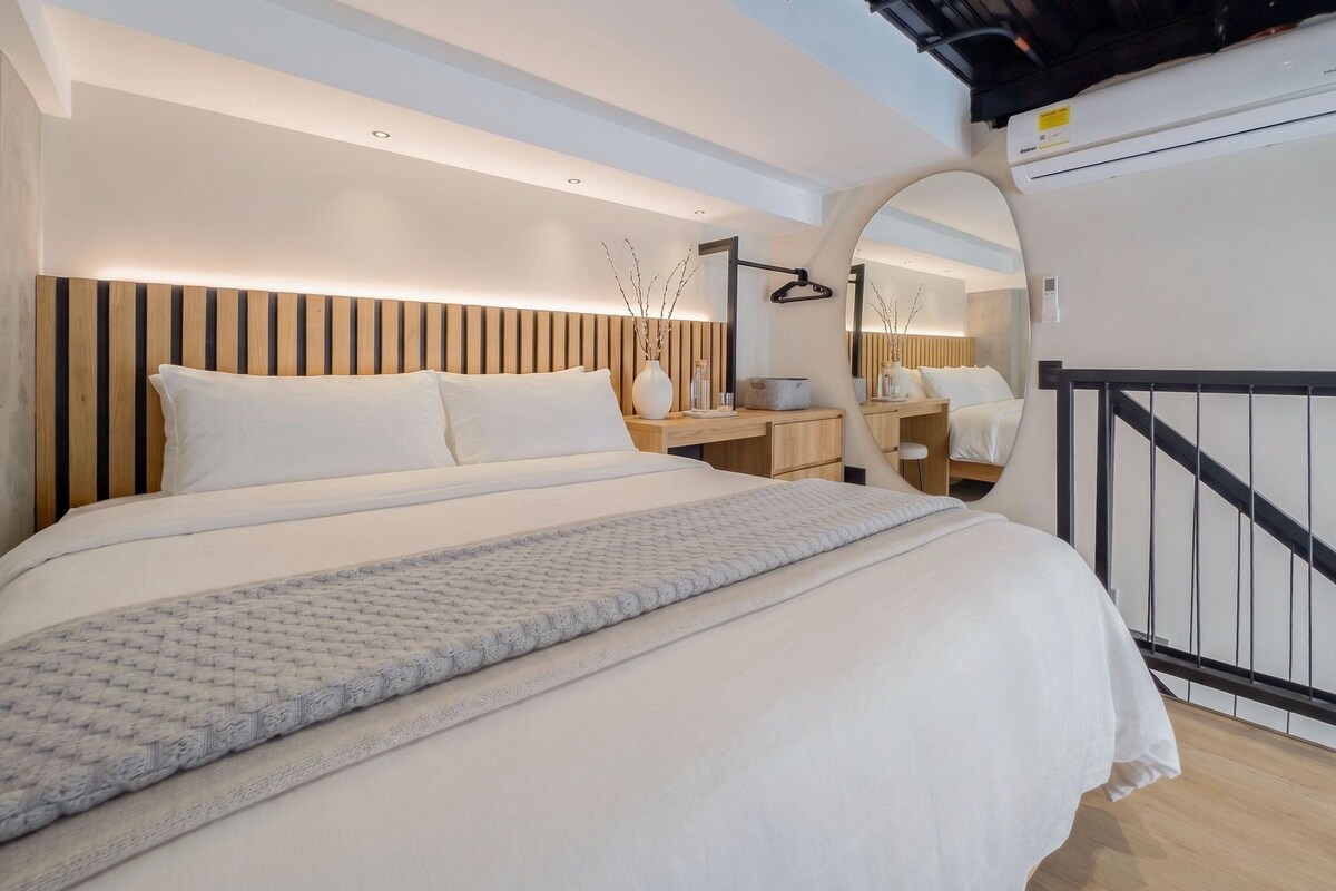 A modern bedroom with a large bed, bedside tables, a mirror, and a ceiling fan.
