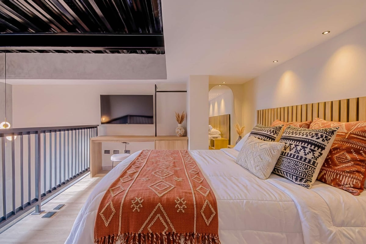A modern bedroom with a large bed, a desk, and a TV.