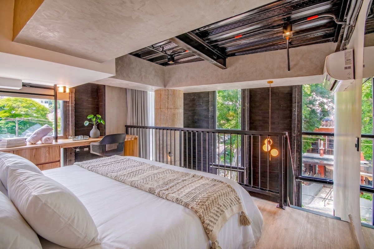 A modern bedroom with a large bed, a desk, and a balcony with a view.