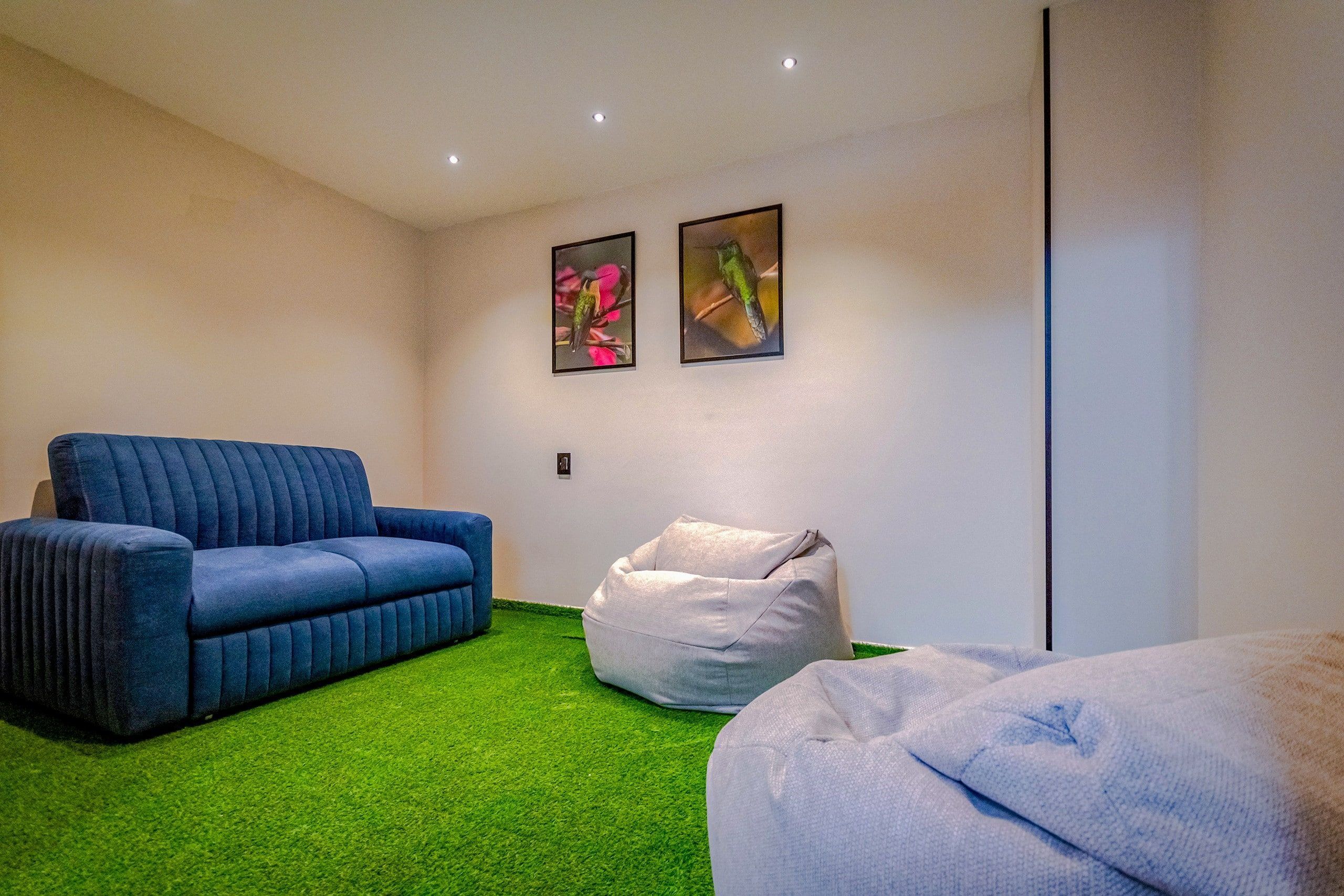 A room with a blue sofa, a white bean bag, and a bed with a white cover. There are two framed pictures on the wall.
