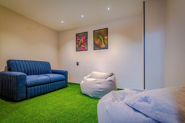 A room with a blue sofa, a white bean bag, and a green carpet.
