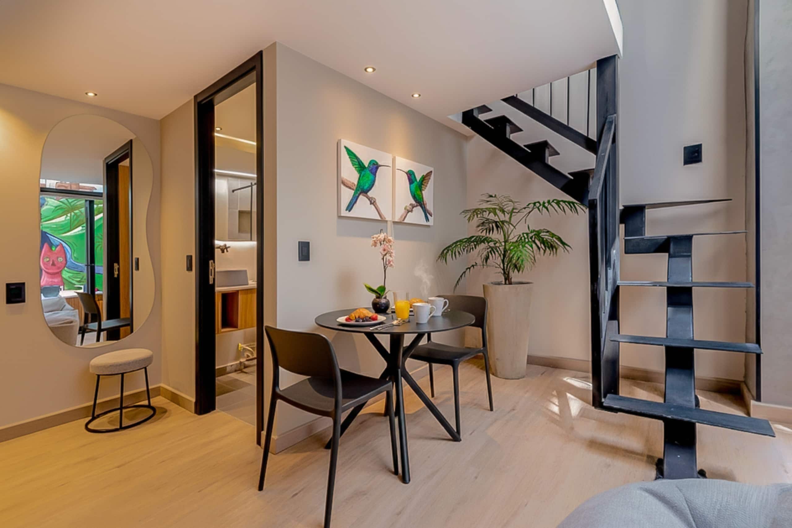 Un interior moderno con zona de comedor, escalera y un espejo grande.
