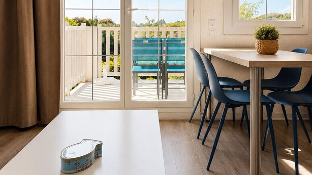 A room with a white table, blue chairs, a white ceiling, and large windows with a view of a balcony and greenery. - Vacation apartment in Bourgenay for 4 people (Talmont-Saint-Hilaire)