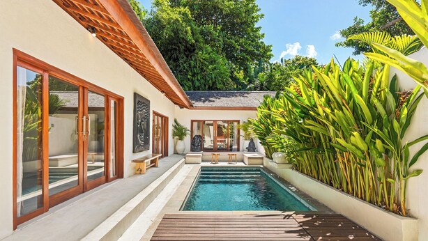 A pool area with a wooden deck, a white wall with a window, and a plant wall. - Tropical Villas Jimbaran (Jimbaran)