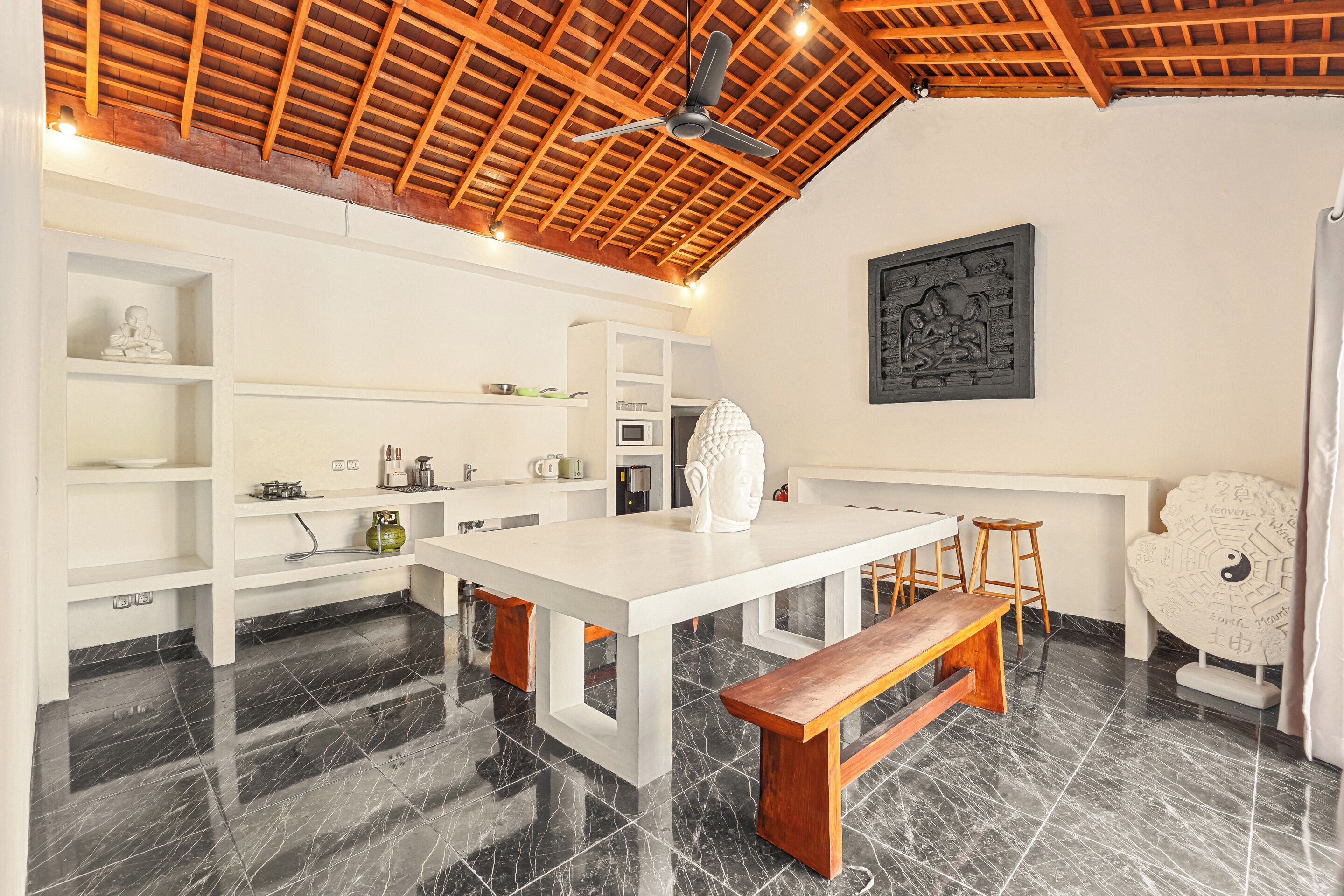 A modern kitchen with a white table, wooden stools, and a ceiling fan.