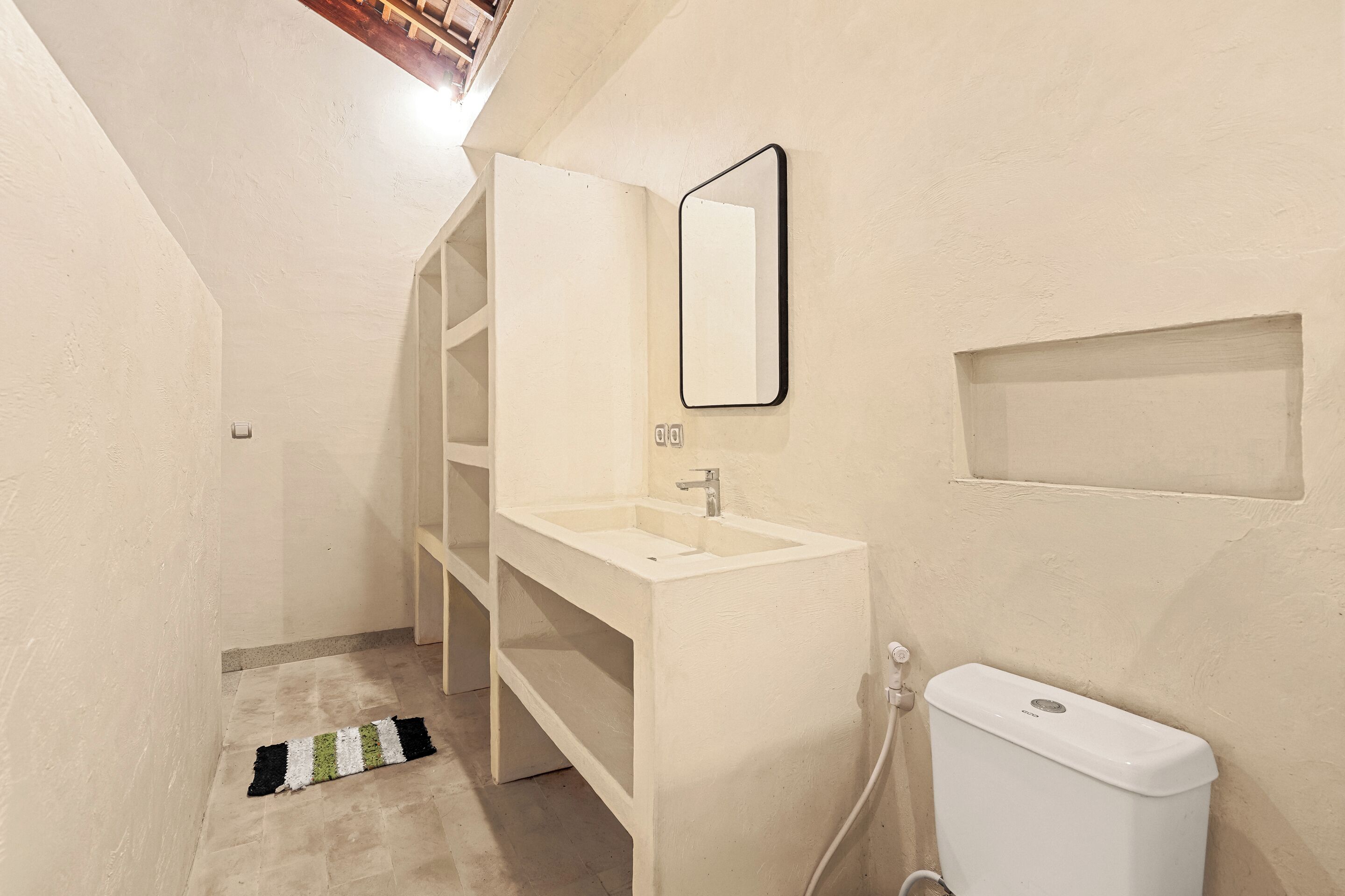 Casa de banho estreita com lavatório branco, espelho e sanita.