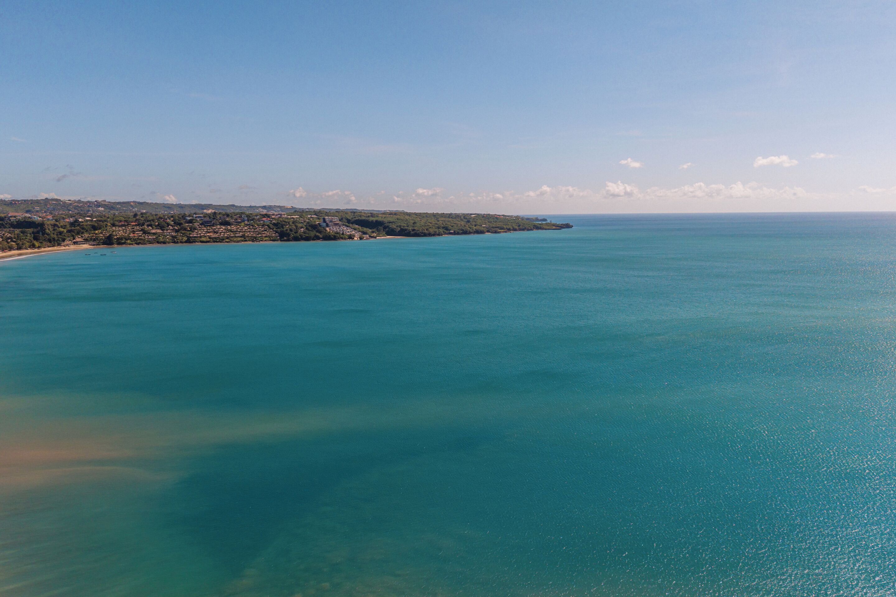 A coastal landscape with a clear view of the sea and a distant shoreline with buildings.