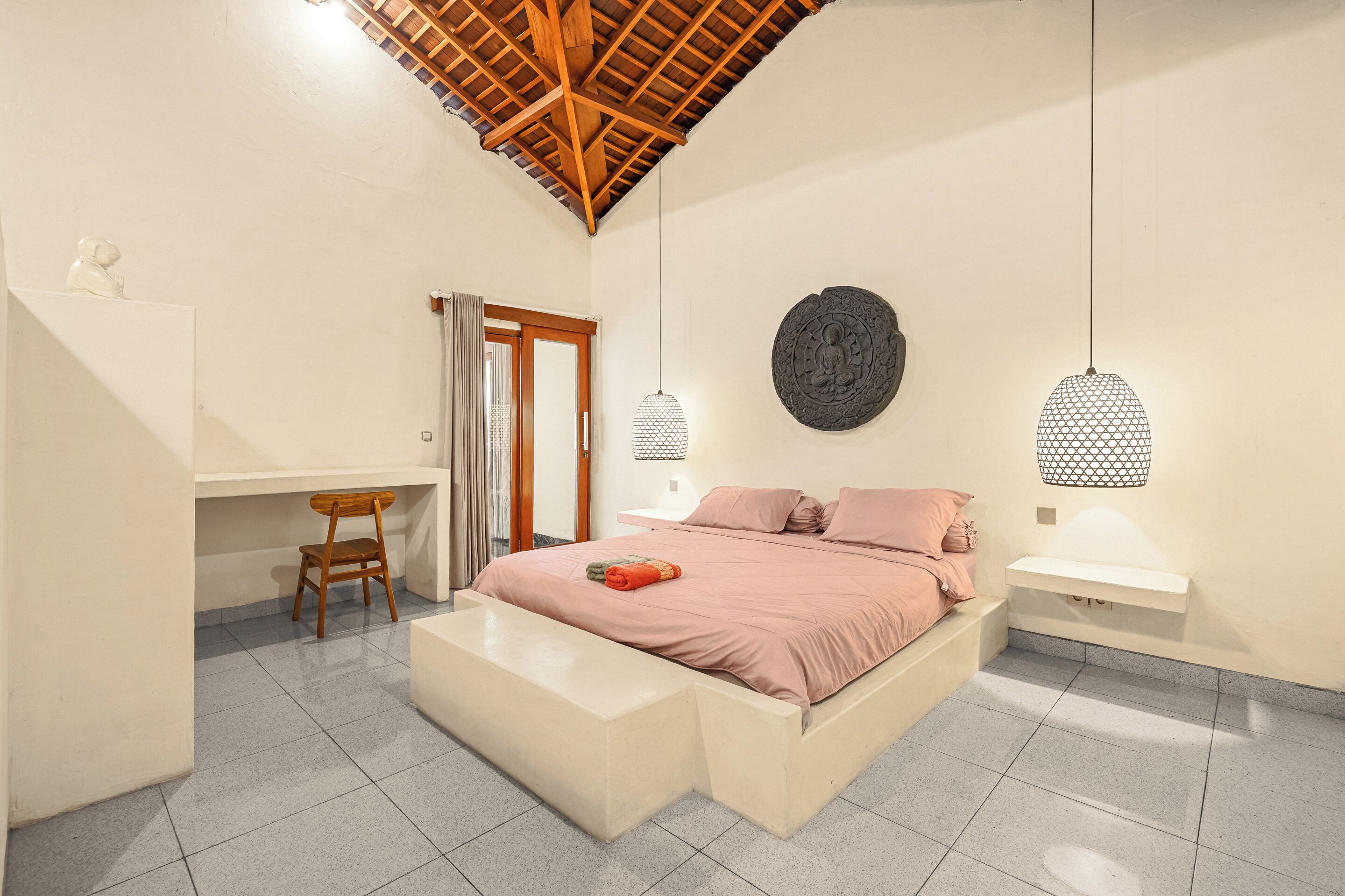 Quarto com cama, escrivaninha, cadeira, banco, prateleira na parede e ventilador de teto.