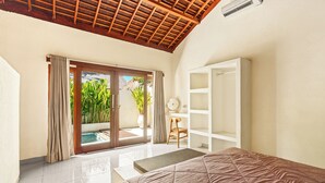 A bedroom with a bed, a white wardrobe, a desk, and a sliding glass door leading to a pool area. - Tropical Villas Jimbaran (Jimbaran)