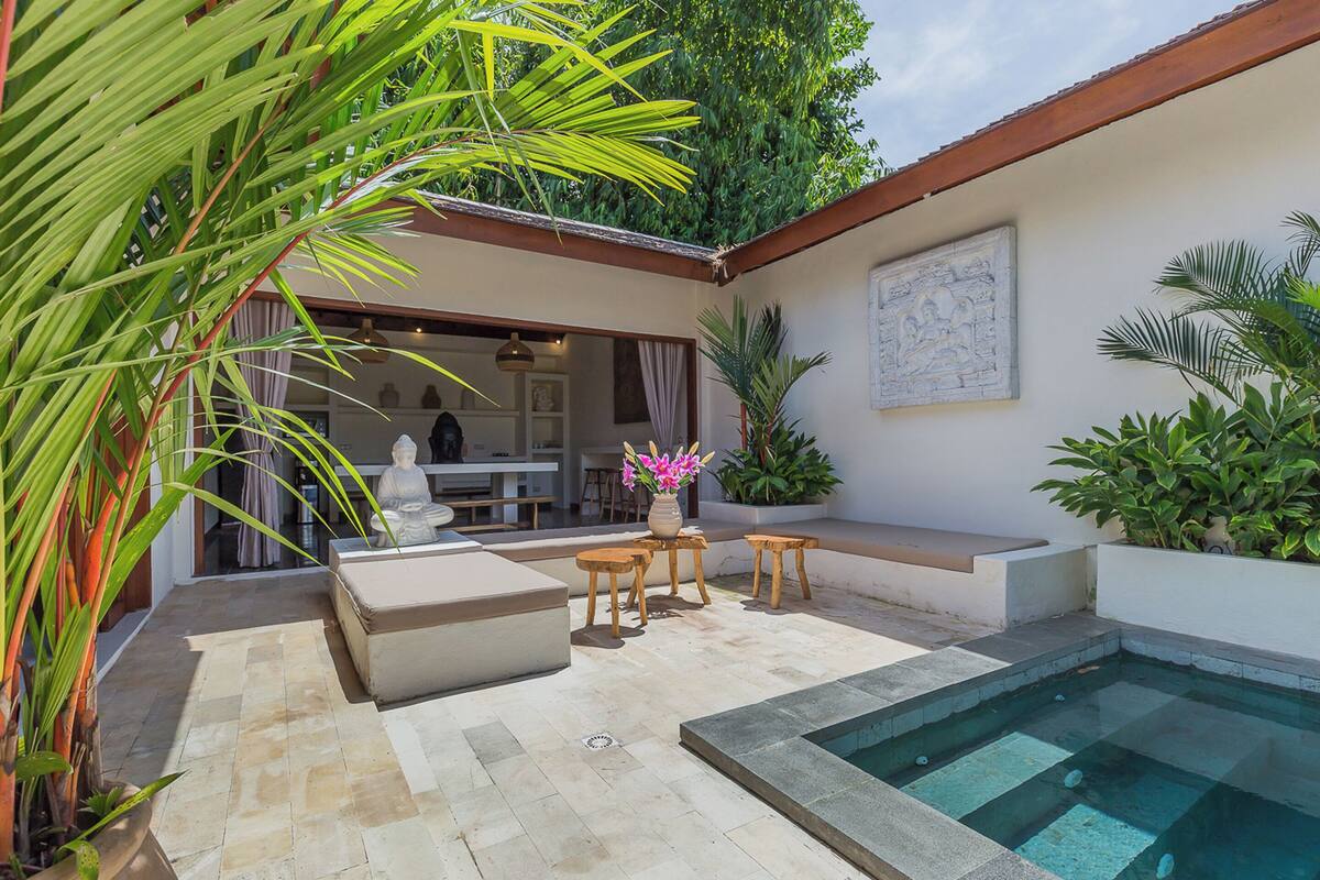 A pool area with a seating arrangement, a statue, and a view into a dining area.