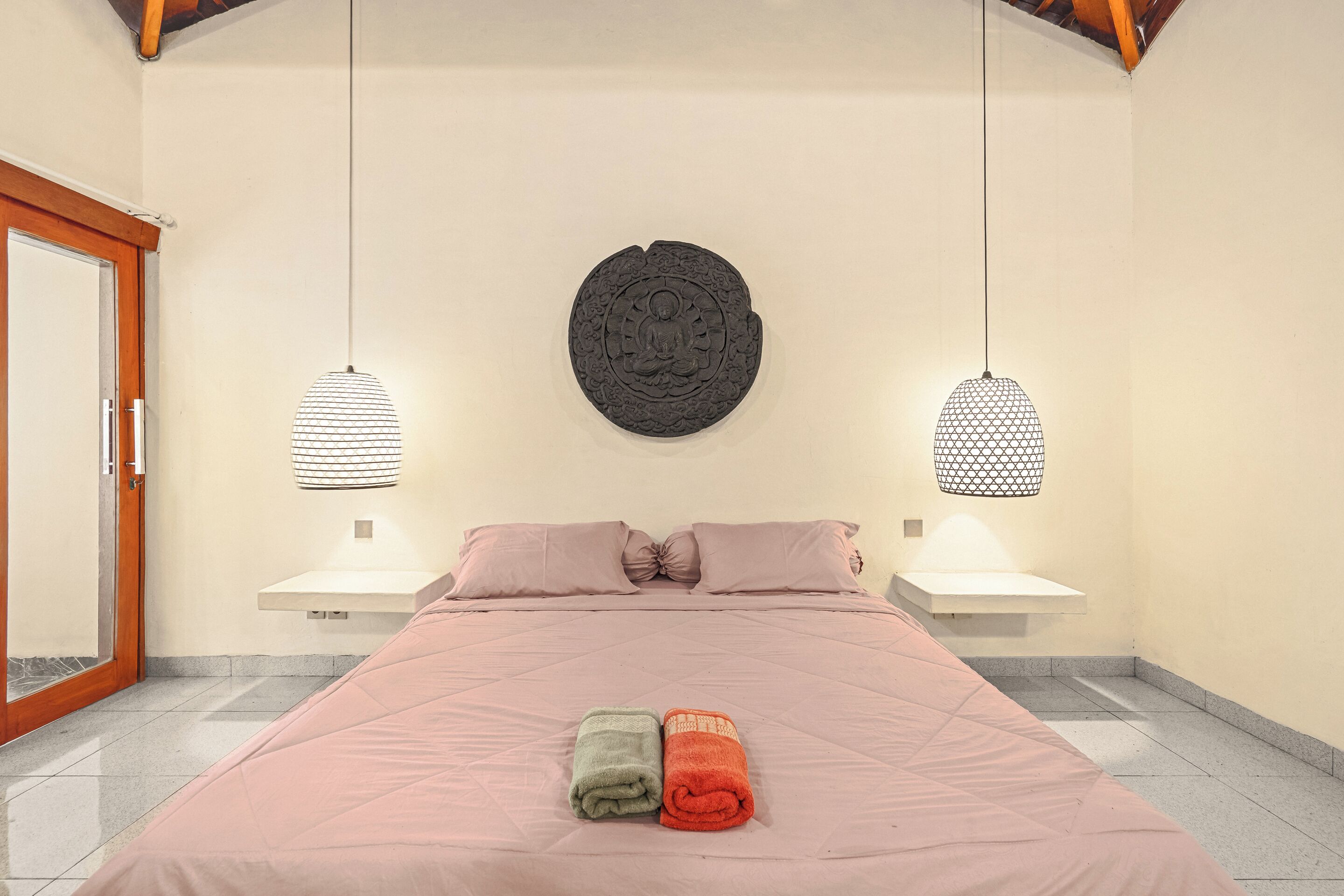 A bedroom with a bed, two bedside tables, a wall-mounted circular decoration, and two hanging lamps.