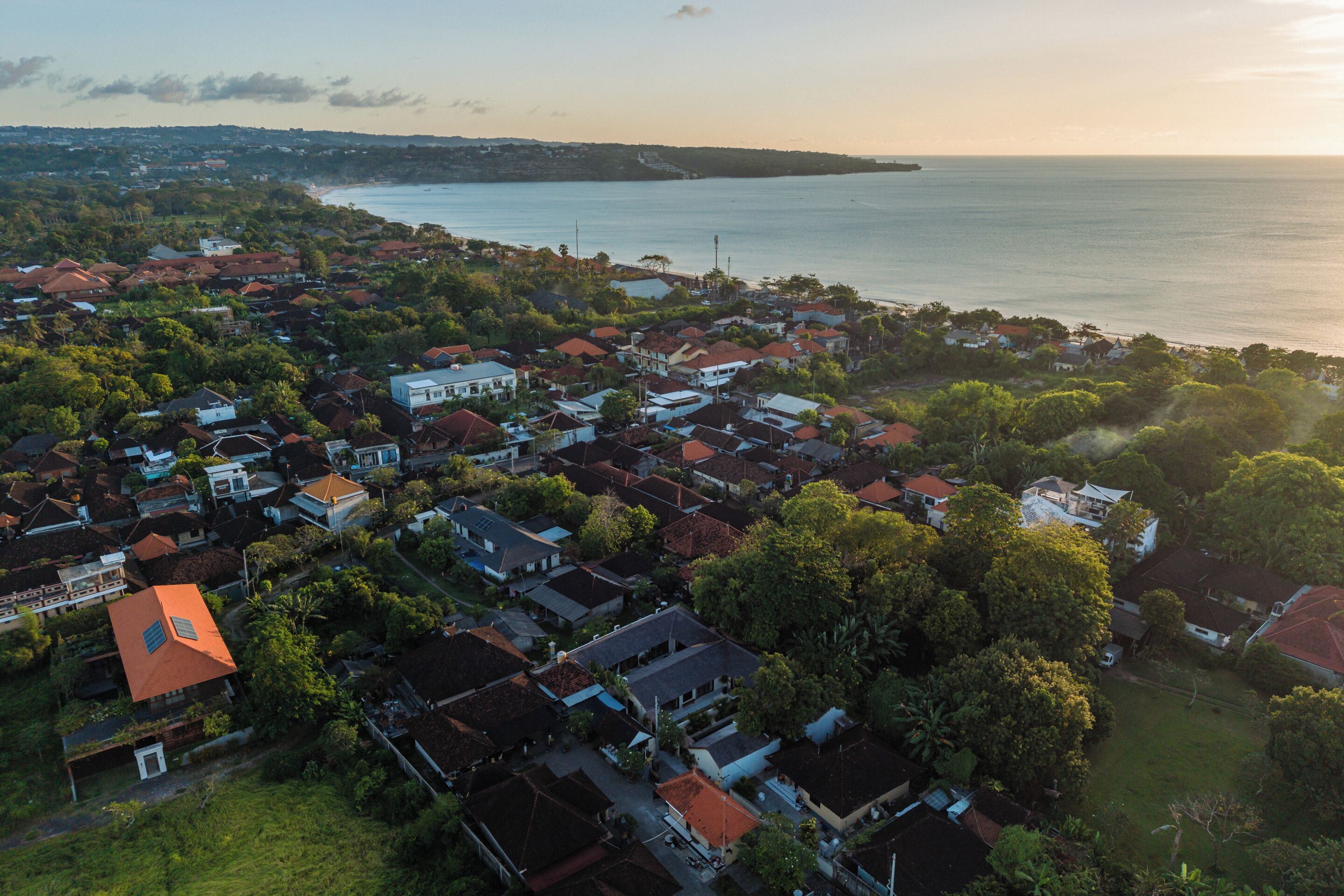 Ett flygbildsbild av ett bostadsområde vid kusten med hus, träd och en strand.