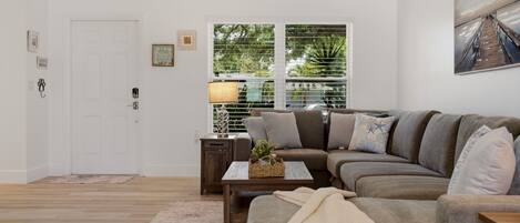 Una sala de estar con un sofá modular, una mesa de centro, una lámpara y vistas al exterior por una ventana.