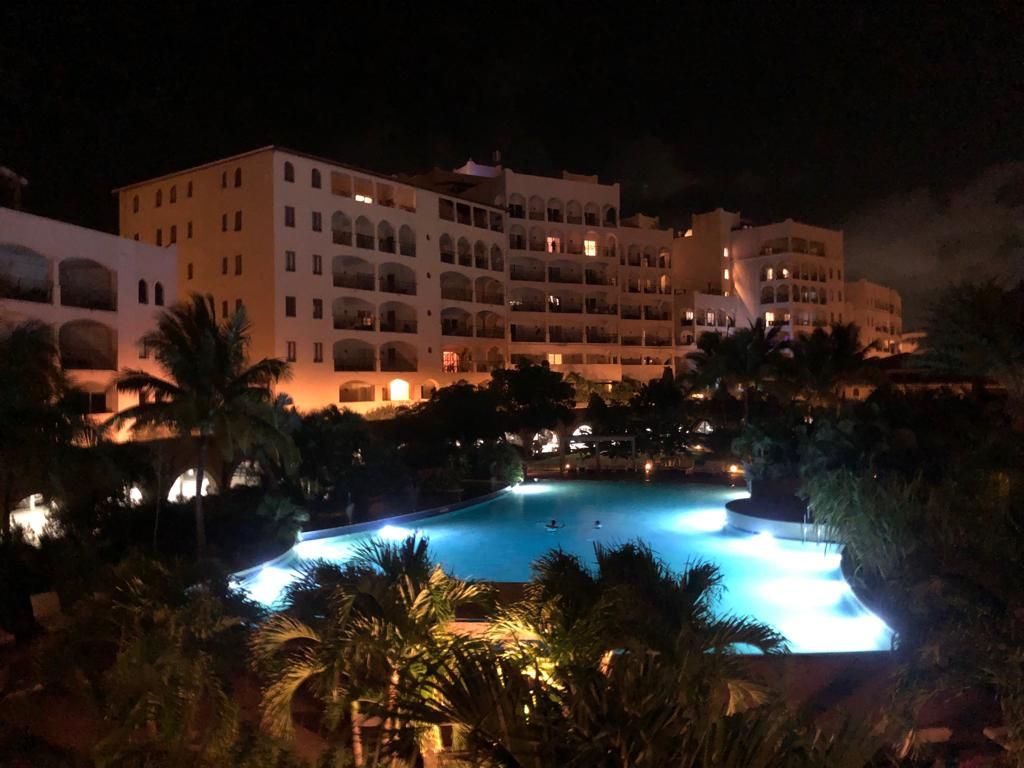 A multi-story hotel with a swimming pool surrounded by palm trees.