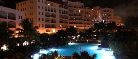A multi-story hotel with a swimming pool surrounded by palm trees.