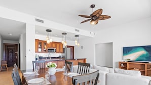 A modern kitchen with wooden cabinets, a dining area with a wooden table and chairs, a ceiling fan, and a large TV on the wall. - Stunning 2 bedroom unit Porto Cupecoy (Cupecoy)