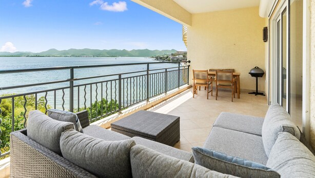 A balcony with a view of the sea, wicker furniture, and a table with chairs. - Stunning 2 bedroom unit Porto Cupecoy (Cupecoy)