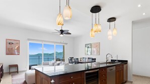 A modern kitchen with a large island, pendant lights, and a view of the sea. - Stunning 2 bedroom unit Porto Cupecoy (Cupecoy)